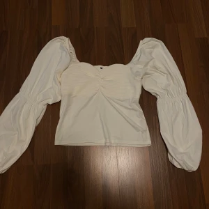 Vit blus med puffärmar - Säljer denna vita / cremefärgade blusen med puffärmar. Har klippt bort lapparna men den är från Bikbok, osäker på storleken men tror S/M. Använt några gngr bara så den är i mycket bra skick! Den har dock en liten smink fläck, vet ej om det går bort i tvätten eller ej