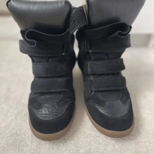 Isabel marant skor - Snygga svarta sneakers med tre breda kardborreband och högre skaft. Skorna har en brun gummisula och är tillverkade i en mix av mocka och syntet. Perfekta för dig som gillar en sportig och trendig look. Helt okay sick därav priset går även int ner i pris då de köptes för 4800!
