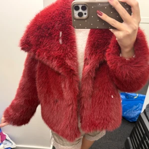 Röd pälsjacka med bred krage - Säljer en supermjuk och fluffig röd pälsjacka med bred krage och lång ärm. Jackan har en cool, lite boxig passform och är perfekt för dig som vill sticka ut. Färgen är intensivt röd och materialet är riktigt mjukt och gosigt.inget varumärke 