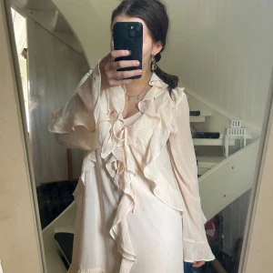 Ljus volangklänning från Xlnt Kappahl - Superfin ljus kortklänning med volanger och knytning fram. Klänningen har långa, vida ärmar och är tillverkad i ett tunt, flowy material som ger en romantisk vibe. Perfekt för dig som gillar en feminin och luftig stil. Kan pruta vid snabbt köp. Använd endast 2 gånger 