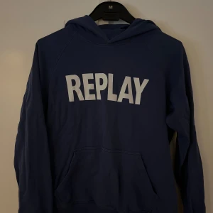 Blå hoodie från Replay med tryck - Snygg marinblå hoodie från Replay med stort vitt tryck på bröstet. Klassisk känguruficka framtill och huva. Perfekt för dig som gillar streetwear och vill ha en bekväm och stilren tröja.