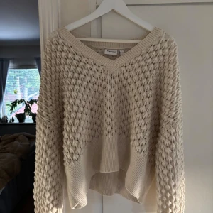 Beige stickad tröja från Kappahl - Säljer en beige stickad tröja från Kappahl med snyggt hålmönster och v-ringad hals. Tröjan har lång ärm, ribbade muddar och en loose fit som ger en chill vibe. Perfekt för lager-på-lager och passar till både jeans och kjol.