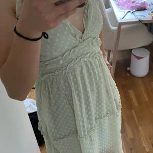 Ljusgrön prickig klänning Vero Moda - Supersöt ljusgrön klänning från Vero Moda med vita prickar, volangdetaljer och smala axelband. Klänningen har omlott-v-ringning och är i ett lätt, luftigt polyestertyg. Perfekt för varma dagar och somriga vibes!