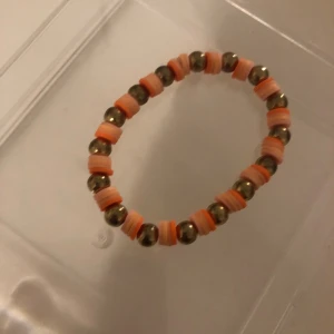 Färgglatt pärlarmband med orange detaljer - Snyggt armband med runda metallpärlor i guld och platta pärlor i olika nyanser av orange. Armbandet är elastiskt och har en lekfull design som sticker ut. Perfekt för dig som gillar färg och vill addera något extra till din stil.