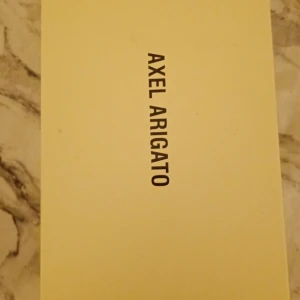 Bruna sneakers från Axel Arigato - Snygga sneakers från Axel Arigato i mocka med klassisk vit sula och mörka snören. Skorna har en stilren och minimalistisk design som passar perfekt till jeans eller chinos. Perfekta för dig som gillar en clean look med premiumkänsla.