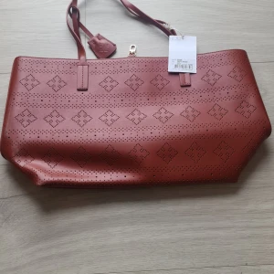 Brun axelväska från By Malene Birger - Snygg brun axelväska från By Malene Birger i skinn med laserutskurna geometriska mönster. Väskan har två smala axelremmar och en tag med logotyp. Perfekt storlek för att få plats med allt du behöver och stilren design som sticker ut.