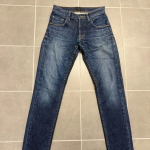 Blå jeans Tiger of sweden 28/32 - Snygga blå jeans från Tiger of sweden i modellen Duce, med klassisk femficksdesign och kontrastsömmar. Jeansen har en smal passform och är tillverkade i slitstarkt denimtyg. Perfekta för dig som gillar en stilren och tidlös look.