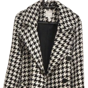Lyxig kappa med bälte - Snygg svartvit kappa med klassiskt hundtandsmönster och stora slag. Kappan har knappar framtill och ett matchande bälte i midjan. Perfekt för dig som vill sticka ut med en trendig och tidlös look. Passar xs-s. Nypris 1499:-