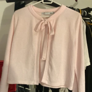 Ljusrosa kofta med knyt i halsen - Supersöt ljusrosa kofta från 157 med knytband i halsen. Mjuk och skön, perfekt för lager-på-lager. Långärmad och i en enkel, klassisk modell som passar till allt. Snygg att styla med jeans eller kjol.