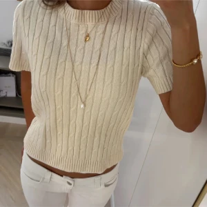 Beige kabelstickad kortärmad tröja - Snygg beige kabelstickad tröja med korta ärmar och rund hals. Tröjan är bara använd ett fåtal gånger så den är som ny<3