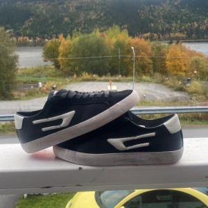 Diesel Low sneakers svart/vit - Säljer ett par svarta och vita Diesel Low sneakers med snygga kontrastdetaljer och röd räfflad sula. Skorna har klassisk snörning och är tillverkade i skinn och syntet. Perfekta för dig som gillar streetstyle och vill sticka ut med coola detaljer. Vid snabb affär kan priset sänkas 
