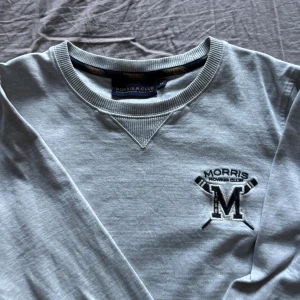 Grå sweatshirt från Morris R Club Herr XS - Ljusgrå sweatshirt från Morris R Club med broderad logga och roddmotiv på bröstet. Tröjan har rund halsringning med ribbade detaljer och långa ärmar. Perfekt för en chill och sportig look.