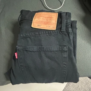 Svarta Levi's 501 jeans W28 L32 - Säljer ett par svarta Levi's 501 jeans i klassisk rak modell. Jeansen har den ikoniska läderpatchen bak och röd Levi's-tag på fickan. Tillverkade i slitstarkt jeanstyg och passar perfekt för en clean och tidlös look.