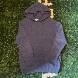 Tröja - En stilren blå hoodie med huva och snörning. Tröjan har långa ärmar och ribbade muddar vid ärmslut och nederkant. Perfekt för en avslappnad look och enkel att matcha med jeans eller joggers.