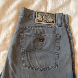 Gråa byxor från Armani Jeans - Snygga gråa byxor från Armani Jeans med klassisk femficksdesign och metallogo på bakfickan. Byxorna har raka ben och normal passform, tillverkade i mjuk bomull. Perfekta för dig som gillar stilrena och tidlösa plagg med exklusiv känsla.