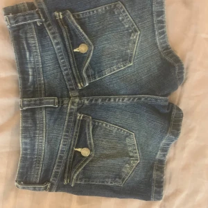 Blå jeansshorts med fickor - Snygga blå jeansshorts med klassisk femficksdesign, tydliga slitningar och kontrastsömmar. Shortsen har bälteshällor, dragkedja och knapp framtill samt lockfickor bak med silverfärgade knappar. Perfekta för en avslappnad stil. Storlek 158 men passar perfekt på mig som är Xs/Xxs 