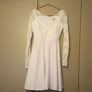 Vit spetsklänning från Goddiva London - Supersöt vit klänning från Goddiva London med långärmade spetsärmar och v-ringad överdel. Klänningen har blommigt spetsmönster upptill och en slät kjol i kort längd. Dragkedja bak för enkel påklädning. helt oanvänd storlek S/M 