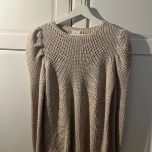 Beige stickad tröja med puffärm - Säljer en beige stickad tröja i storlek S med rund hals och puffärmar. Tröjan har en ribbad struktur och är glittrig. Den är beställd ifrån boozt men märket är the new.
