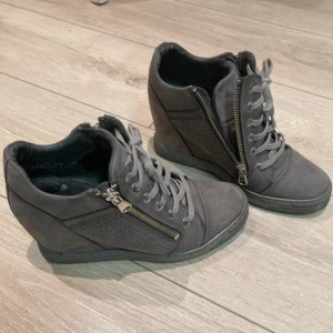 Kilklackade sneakers  - Säljer ett par unika grå sneakers med kilklack, snörning och dragkedja på sidan. Skorna är i skinn med perforerade detaljer på sidorna och har en rund tå. Perfekta för dig som vill ha lite extra höjd men ändå en sportig look💗