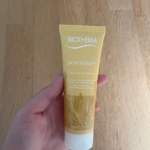 Biotherm Bath Therapy Delightning Blend - En gul tub med Biotherm Bath Therapy Delightning Blend, en återfuktande kroppskräm med doft av grapefrukt och salvia. Tuben rymmer 75 ml och har ett stilrent, tropiskt mönster. Perfekt för dig som gillar fräscha och fruktiga dofter.