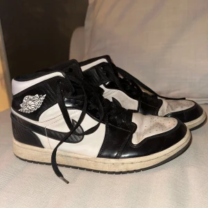 Nike Jordan svartvita sneakers - Säljer ett par klassiska Nike Jordan sneakers i svart och vitt. Skorna har högt skaft, svart snörning och den ikoniska Jordan-loggan på sidan. Ovandelen är i skinn med perforerad tåbox och svart Swoosh. Perfekta för dig som gillar streetstyle och vill sticka ut. Skorna är äkta. Köpta för ca 2500kr