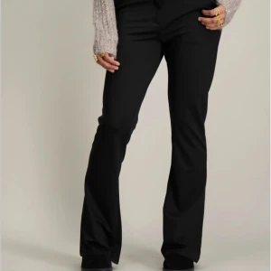 Svarta bootcut kostymbyxor - Svarta kostymbyxor med bootcut-silhuett och klassisk midja. Byxorna har hällor för bälte och stängs med knapp och dragkedja. Perfekta för en clean och stilren look, passar till både stickad tröja och skjorta.