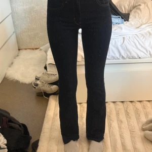 Levi's 725 High Rise Bootcut Jeans - Mörkblå Levi's 725 high rise bootcut jeans med klassiska kontrastsömmar och femficksdesign. Hög midja och bootcut-ben ger en snygg siluett. Tillverkade i stretchigt jeansmaterial för skön passform. Perfekta för dig som gillar en tidlös och trendig look.