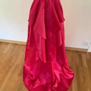 Röd långklänning med volanger - Snygg röd långklänning med flera lager volanger och glansigt tyg som ger en lyxig känsla. Perfekt för dig som vill sticka ut med en dramatisk och elegant look. Klänningen har en klassisk passform och faller vackert längs kroppen.