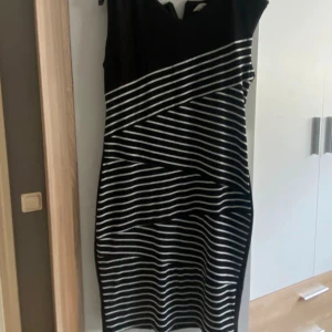 Svartvit randig klänning Makiyo M - Snygg svart klänning från Makiyo i storlek M med vita diagonala och horisontella ränder. Klänningen är ärmlös och har en kroppsnära passform som framhäver siluetten. Perfekt för dig som gillar grafiska mönster och stilren design.