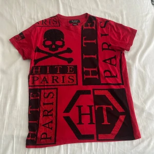 Röd t-shirt HITE Couture med döskalle - Röd t-shirt från HITE Couture med svart döskalletryck och stora textdetaljer med 'PARIS' och 'HITE' i olika rutor.