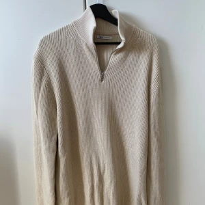 Beige stickad half zip-tröja från Zara - Säljer en beige stickad tröja från Zara med half zip och hög krage. Tröjan har lång ärm och är ribbstickad för en snygg och avslappnad look. Perfekt för lager-på-lager under kyliga dagar.