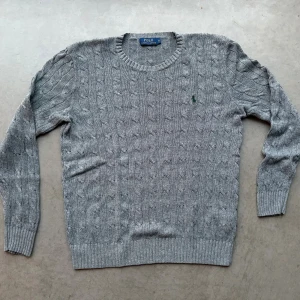 Kabelstickad tröja Polo Ralph Lauren - Tunnt kabelstickad mörkgrå tröja från Polo Ralph Lauren i bomull. Storleken är herr S