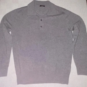 Grå polotröja från Massimo Dutti - Snygg grå polotröja från Massimo Dutti i mjuk ullblandning. Tröjan har klassisk krage, tre knappar framtill och långa ärmar. Perfekt för lager-på-lager och stilrena outfits.