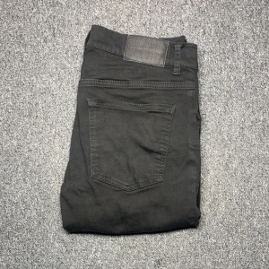 Svarta jeans från J.Lindeberg 31/32 - Svarta jeans från J.Lindeberg med klassisk femficksdesign och diskret logga på bakfickan. Jeansen har en rak passform och är tillverkade i ett mjukt bomullsmaterial med lite stretch för extra komfort. Perfekta för en stilren och avslappnad look.