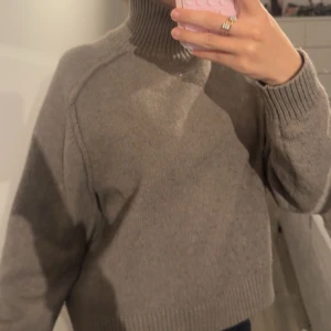 Grå stickad från H&M - Mysig grå polotröja från H&M med ribbad hög krage och muddar. Tröjan är stickad och har en loose fit med långa ärmar. Perfekt för kyliga dagar och enkel att matcha med jeans eller kjol.