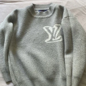 Grå stickad tröja från Louis Vuitton - Säljer en grå stickad tröja från Louis Vuitton med stort vitt LV-logo storlek L men sitter mer som M-S