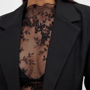 Svart spetsblus från NA-KD - Säljer en transparent svart spetsblus från NA-KD med lång ärm. Blusen har ett tunt meshmaterial med blommigt spetsmönster och är figurnära. Perfekt att styla lager på lager eller med ett snyggt linne under.