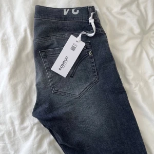 Dondup George - Snygga helt nya Dondup George skinny fit jeans i mörkgrå tvätt med klassisk femficksdesign och silverfärgade knappar. Jeansen har en diskret D-logga vid bakfickan och är tillverkade i stretchig bomull. Köpta för 3799 och är aldrig använda, jag på bilden är 182,77kg, hör av er vid funderingar