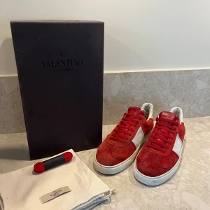 Valentino Garavani röda sneakers - Snygga röda och vita Valentino Garavani sneakers i mocka och skinn. Extremt eftertraktadade i sånt här bra skick! Allt OG medföljer, alla nitar kvar utom en som man kan se på bild 5! Storlek 43! Pris 3799kr!!
