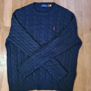 Mörkblå kabelstickad tröja Polo Ralph Lauren - Kabelstickad mörkblå tröja från Polo Ralph Lauren. Köpte för någon vecka sedan och har endast använt den ett fåtal gånger då den sitter för stort på mig. Utmärkt skick.