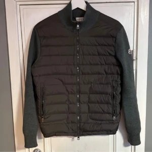 Grå moncler cardigan  - Snygg grå pufferjacka från Moncler med quiltad front och stickade ärmar. Jackan har dragkedja framtill, två dragkedjefickor och ribbade muddar. Klassisk Moncler-logga på ärmen och hög krage för extra stilpoäng. Skriv vid mer frågor 
