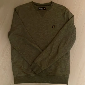 Grå/Grön sweatshirt - Säljer en stilren grå/grön sweatshirt från Lyle & Scott med klassisk rund hals och deras ikoniska gula fågel-logga broderad på bröstet. Skick 9/10. Storlek M men passar bra på S. Skriv vid minsta fundering!