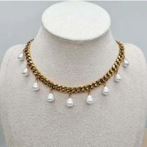 Guldhalsband med droppformade pärlor - Unikt halsband i guldtonad kedja med hängande droppformade vita pärlor. Kedjan är chunky och ger en cool statement-look, medan pärlorna tillför en elegant touch. Perfekt för dig som gillar att sticka ut med snygga detaljer.