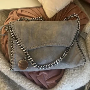 Stella mc liknande väska - Stella McCartney liknande väska i mocka med silverfärgad kedja runt kanterna och som axelrem. Väskan har ett leopardmönstrat innerfoder och magnetlås. 