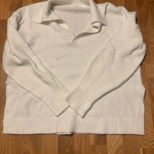 Vit polotröja med krage från Lager 157 - Kolla in denna vita polotröja från Lager 157! Den har en snygg krage, v-ringad öppning och ribbade muddar vid ärmslut och nederkant. Tröjan är i mjuk akrylblandning med polyester och lite elastan för extra komfort. Perfekt för lager-på-lager under kyliga dagar.