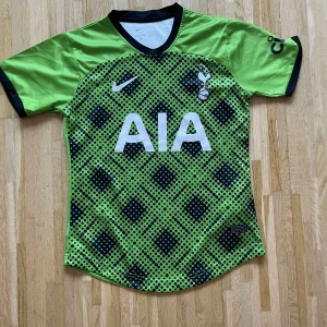 Tottenham Hotspur grön bortatröja Nike - Säljer en grön Tottenham Hotspur bortatröja från Nike med svart och mörkgrönt rutmönster framtill. Tröjan har korta ärmar, svart krage och vita logotyper. Materialet är lätt och andas, perfekt för fotbollsträning eller match.