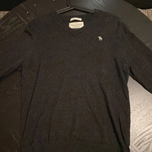 Mörkgrå kashmirtröja Abercrombie M - Mysig mörkgrå tröja från Abercrombie & Fitch i kashmirblandning. Klassisk v-ringning och diskret logga på bröstet. Perfekt för lager-på-lager och passar till allt. Långärmad och riktigt skön att ha på sig.