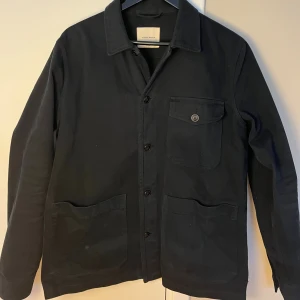 Mörkblå jacka från A Day's March - Säljer en mörkblå jacka/overshirt från A Day's March i storlek medium. Jackan har tre fickor framtill, knäppning med knappar och klassisk krage. Perfekt att slänga över en t-shirt för en clean och stilren look.