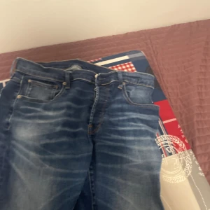 Blå skinny jeans med slitningar - Säljer ett par blå skinny jeans med snygga slitningar och tvättade detaljer. Jeansen har klassisk femficksdesign, smal passform och normal midja. Perfekta för dig som gillar en modern och stilren look.