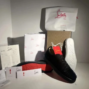 Christian Louboutin svarta sneakers med nitar - Svarta sneakers från Christian Louboutin med klassisk röd sula och coola svarta nitar på tån. Skorna har snörning och är tillverkade i en mix av skinn och mocka. Perfekt för dig som vill sticka ut med exklusiv design och edgy detaljer.